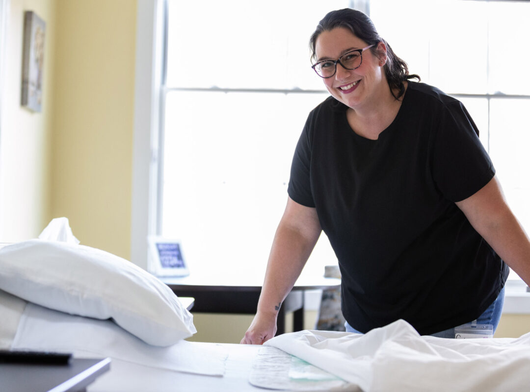 A lady smiling at the camera while she is making a bed at Pappus House.