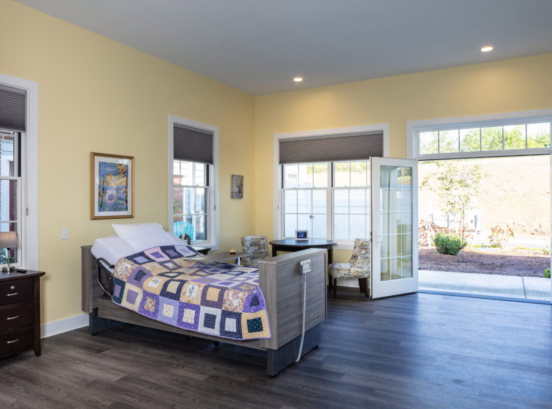 A yellow painted bedroom in Pappus House with lots of big windows and a bed on one side. The doors are open to a patio.