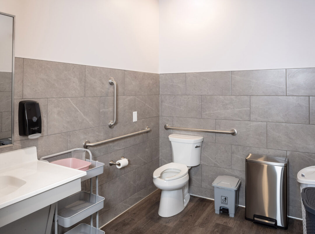 a tiled bathroom with wood grain floor and gray wall tiles.