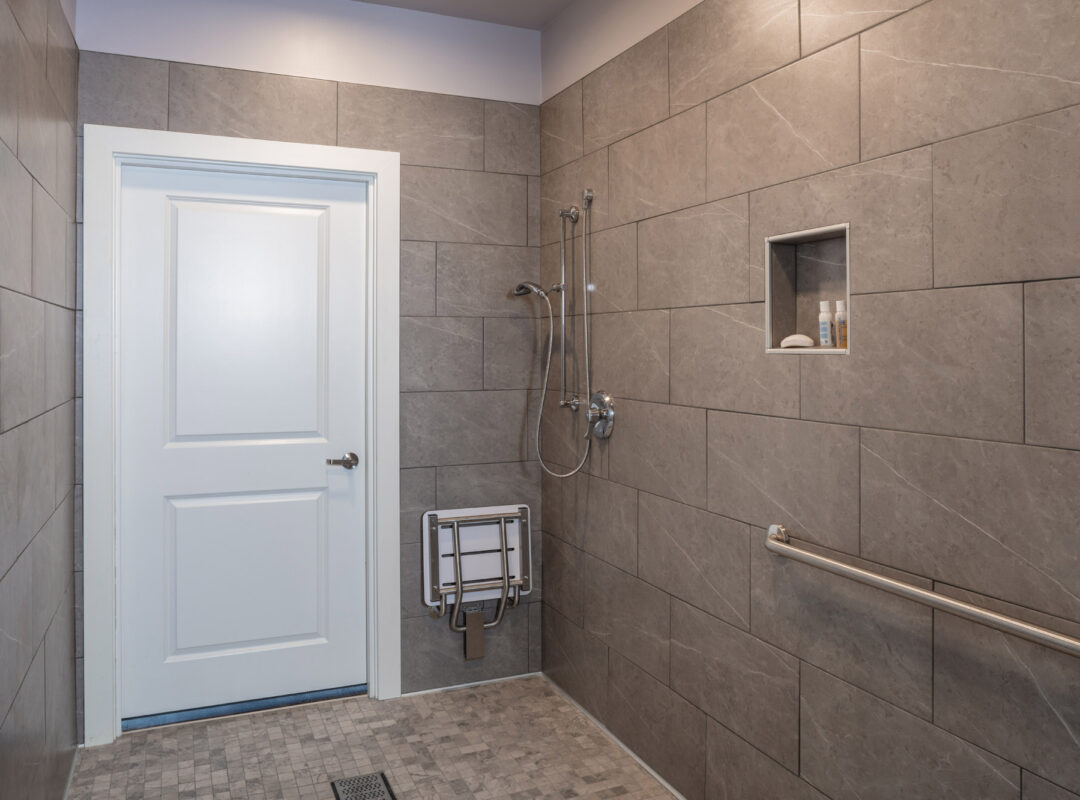 A tiled bathroom with small tiled floor, a shower, and gray wall tiles.