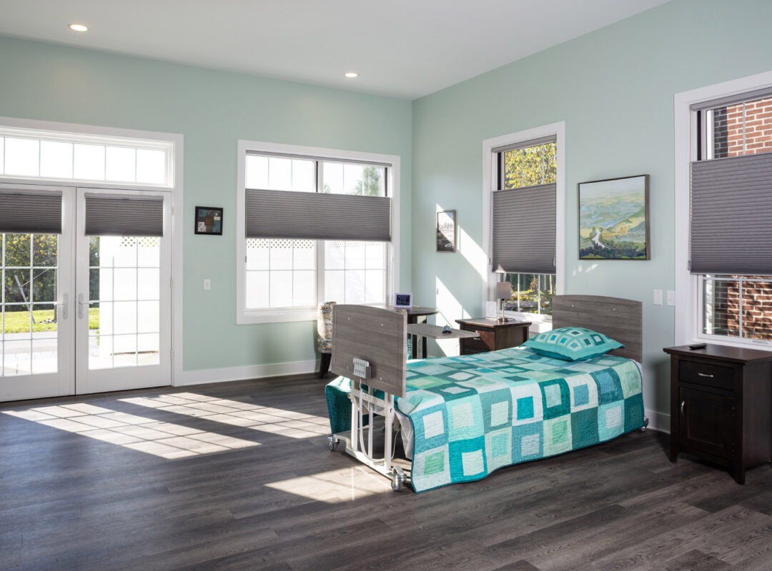 A green painted bedroom in Pappus House with lots of large windows and a bed on one side.