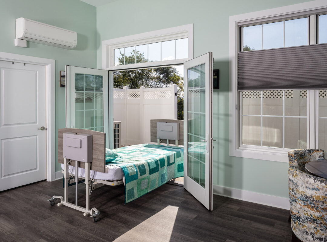 A green painted bedroom in Pappus House with the doors open to the patio and the bed halfway out the door.