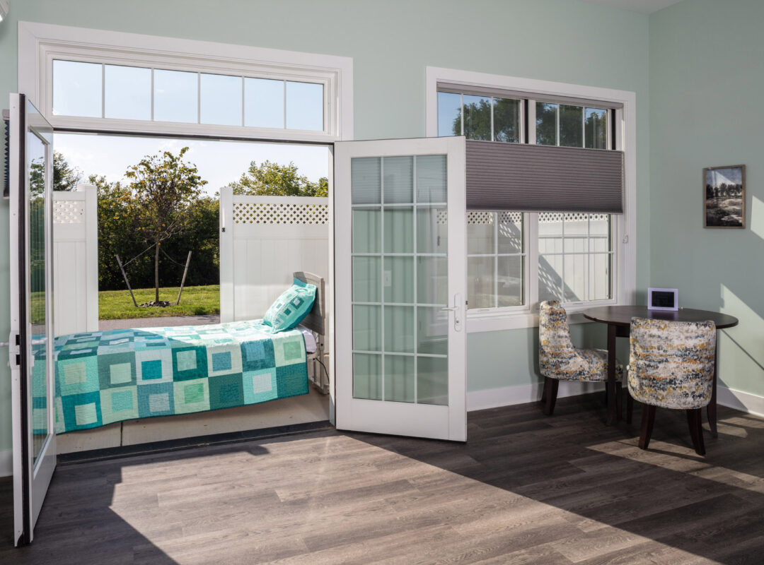 A green painted bedroom in Pappus House with the doors open to the patio and the bed on the patio in the sun.