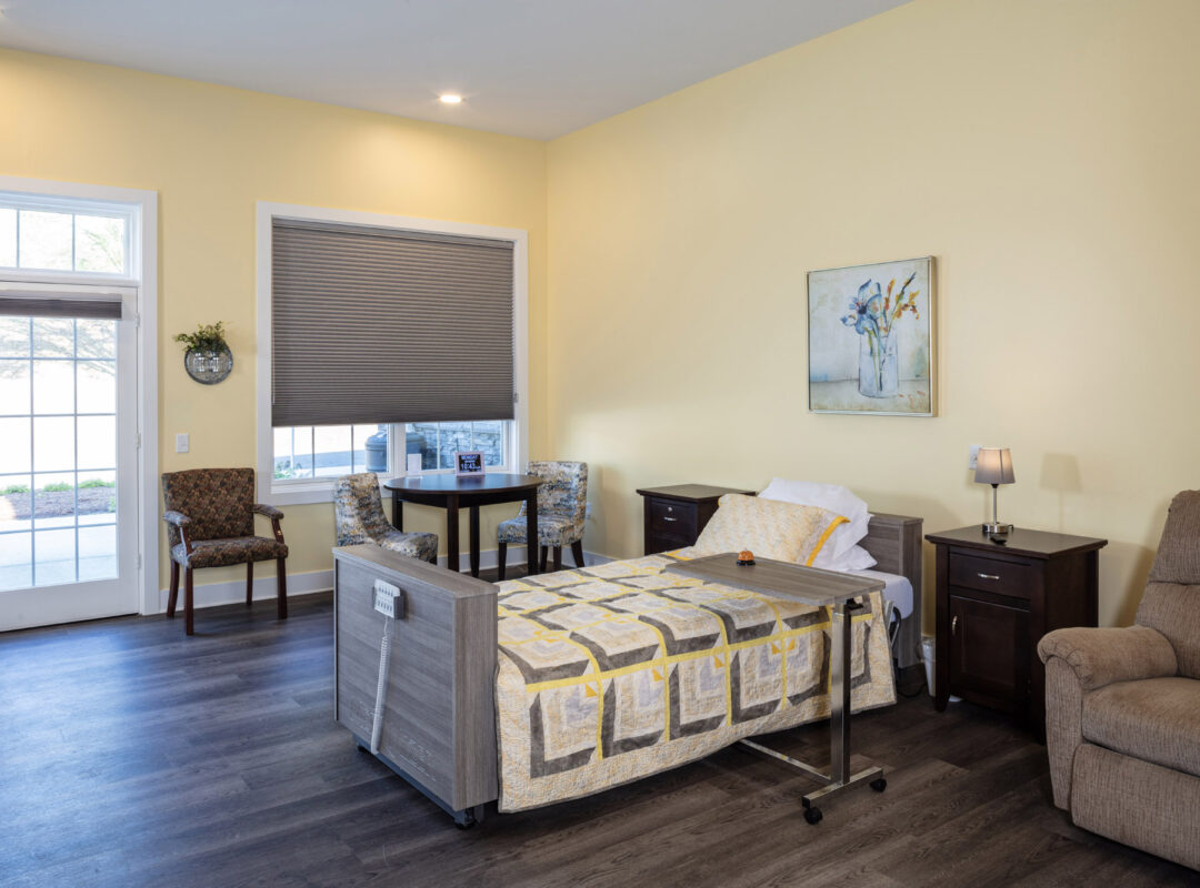 A yellow bedroom with lots of windows, a bed, desk, chairs, and a sofa.