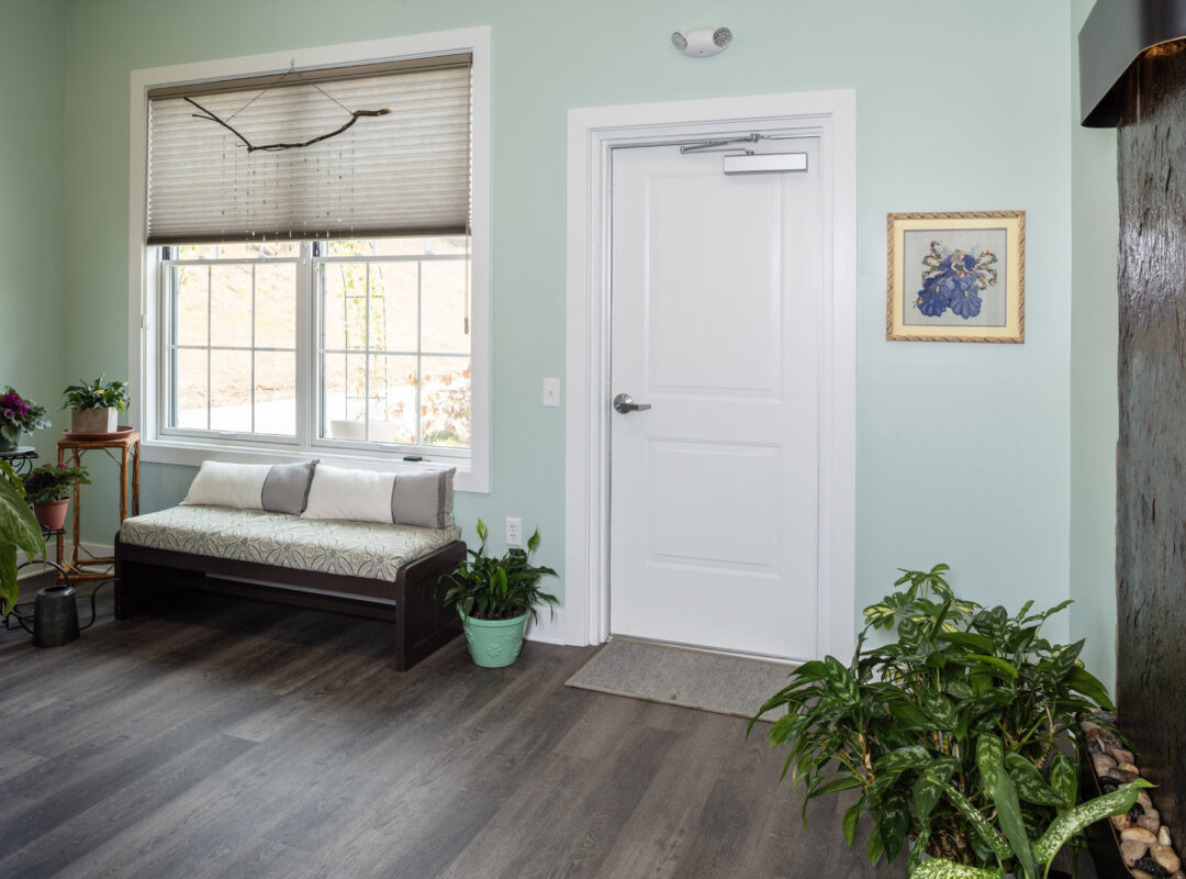 A green room in Pappus House with an outside door, a water feature, and a couch under the window.