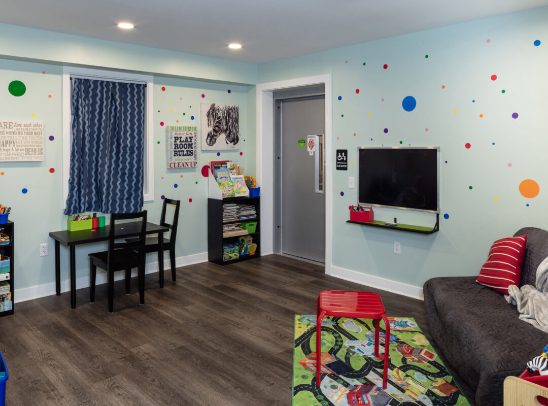 A green painted room with a couch and kids toys, colorful dots on the walls, and a chalk board on the wall.